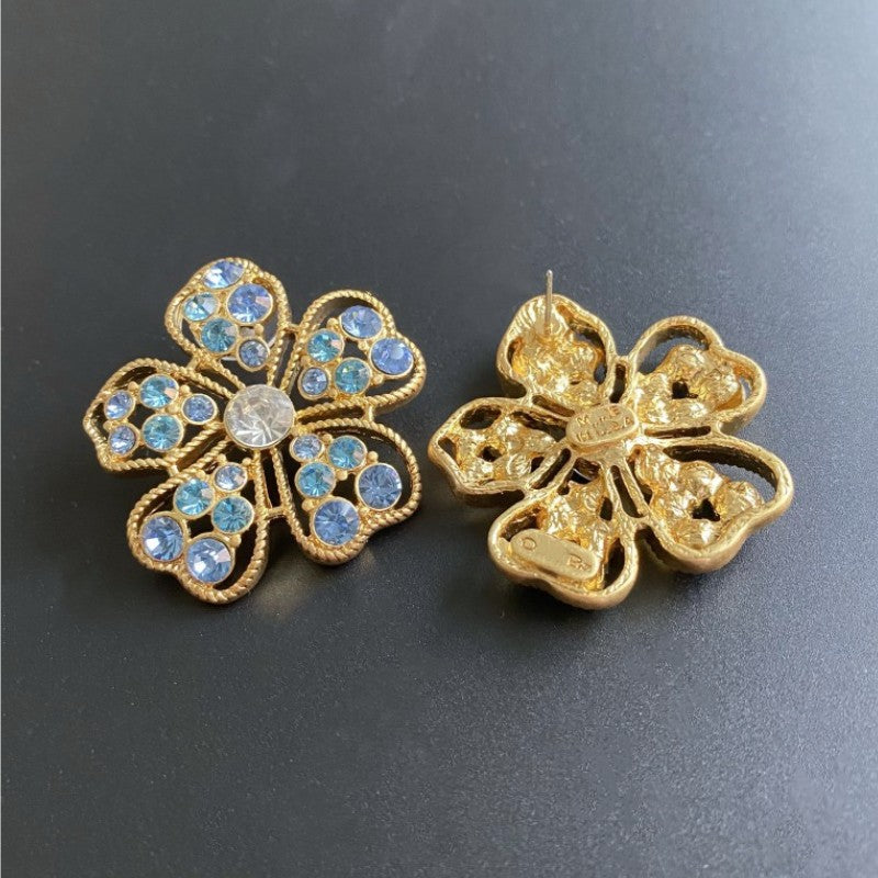 Floral stud earrings with blue pavé stones and gold-tone openwork petals; one shows back