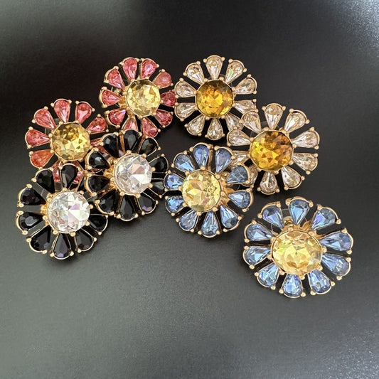 Sunburst flower stud earrings with mixed black, clear, and blue stones; yellow center.