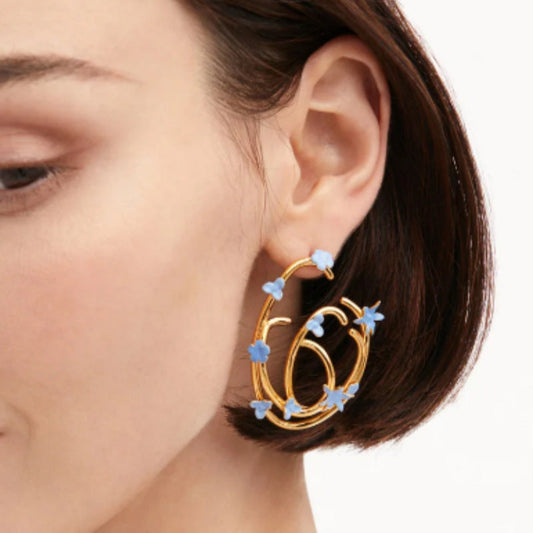 Gold-tone hoop earrings with blue enamel flower charms, seen on ear