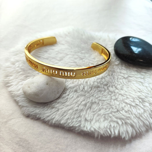 Gold logo cuff bangle on white plush, open band with cutout miumiu text