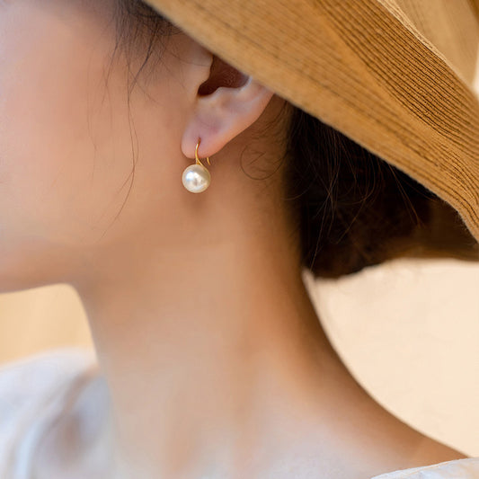 Round pearl hook earrings on ear with gold-tone hooks and white round pearls