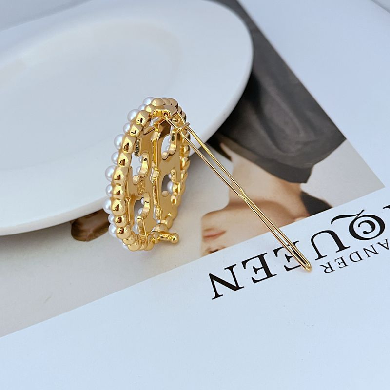 Gold hair clip with white pearl rim and two prong pins, side view