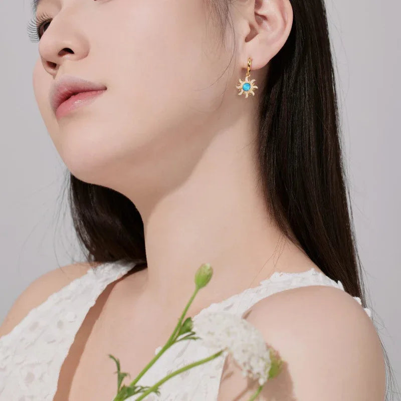 Gold sun hoop earrings with blue round gemstone and sunburst charm, side profile