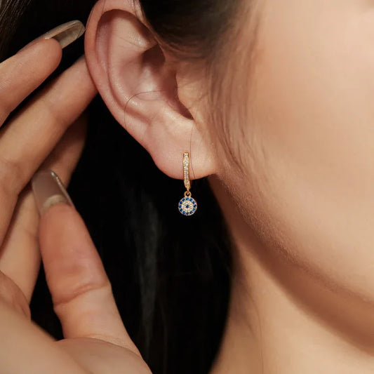 Gold hoop earring with blue evil-eye round charm and clear stones, worn on ear