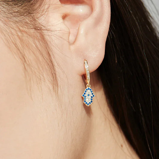 Gold hoop earring with blue hamsa evil eye charm and clear stones on ear