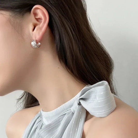 White gold interlaced fold hoop stud earring, close-up on ear