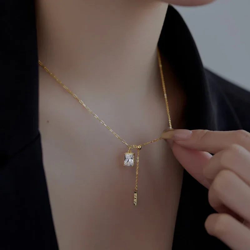 Gold-plated square CZ pendant necklace with vertical bar charm being held near the collar