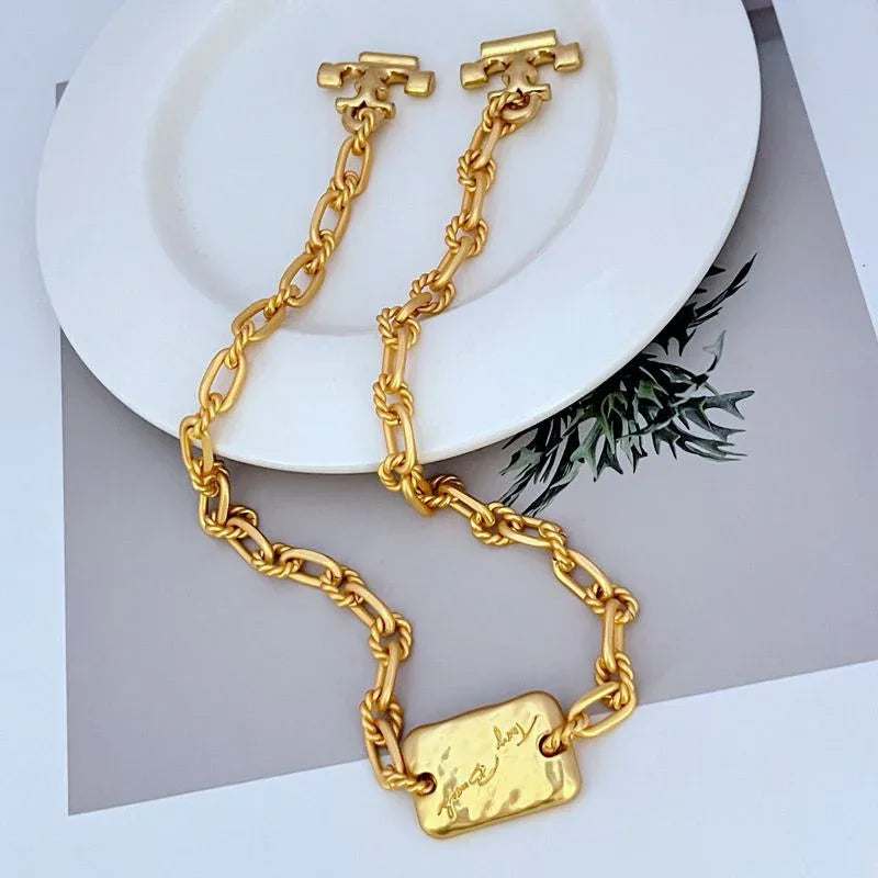 Gold-tone chunky chain bracelet with rectangular metal tag and Tory Burch logo charms.