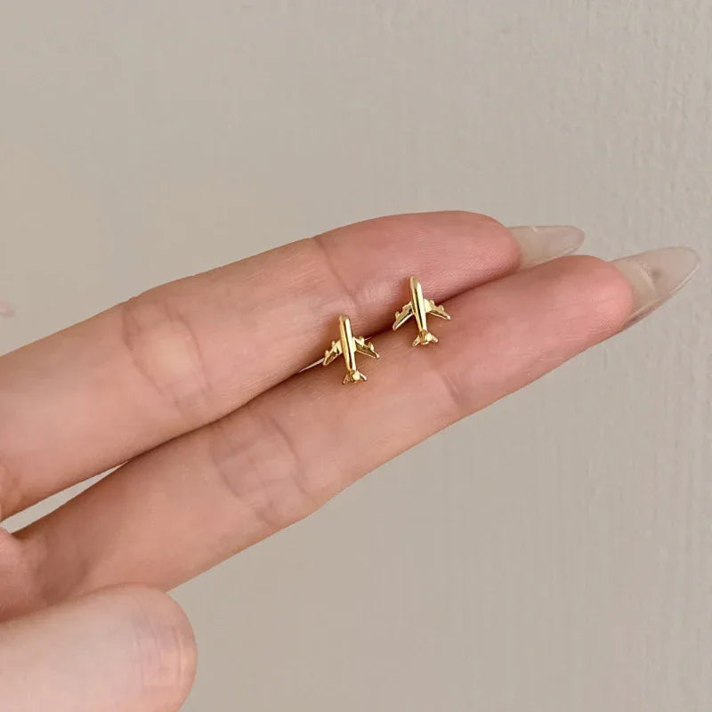Gold airplane stud earrings held in hand, butterfly backs visible