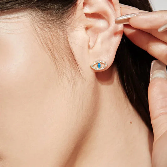 Evil eye stud earrings with blue teardrop center and clear stone halo, worn on ear.