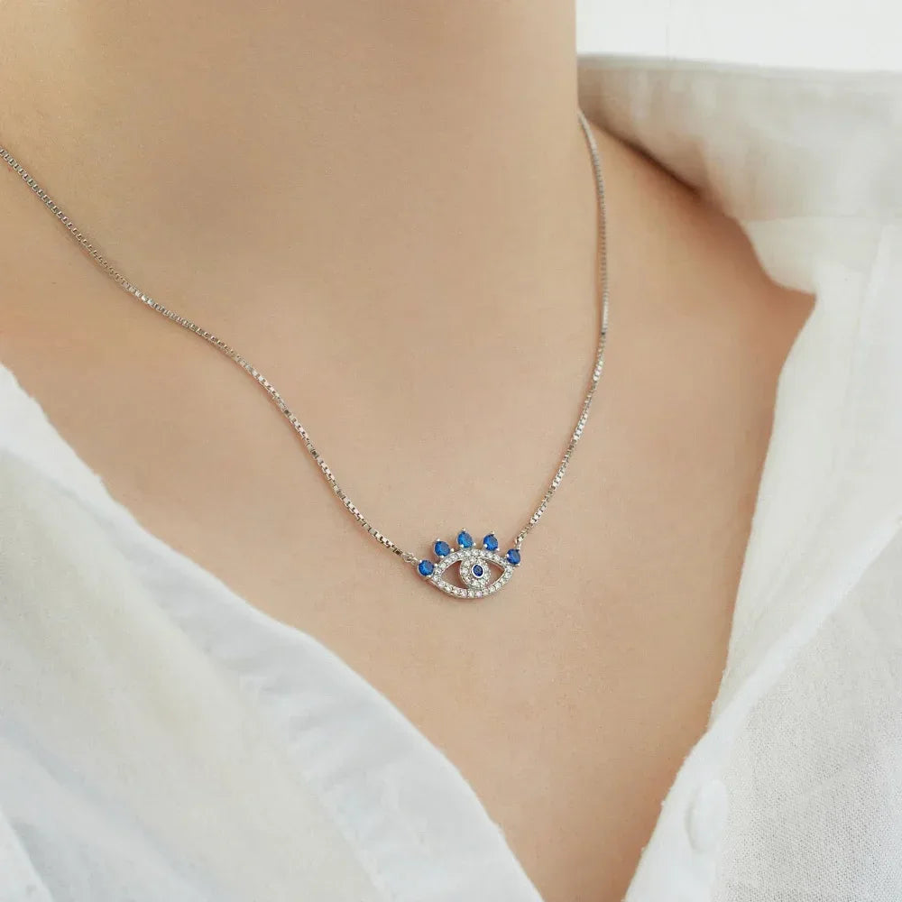 Silver evil eye pendant necklace with blue stones and crystal border, on neck