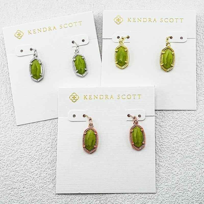 Kendra Scott cat's eye drop earrings with green oval stones in silver, gold, and rose-gold tones