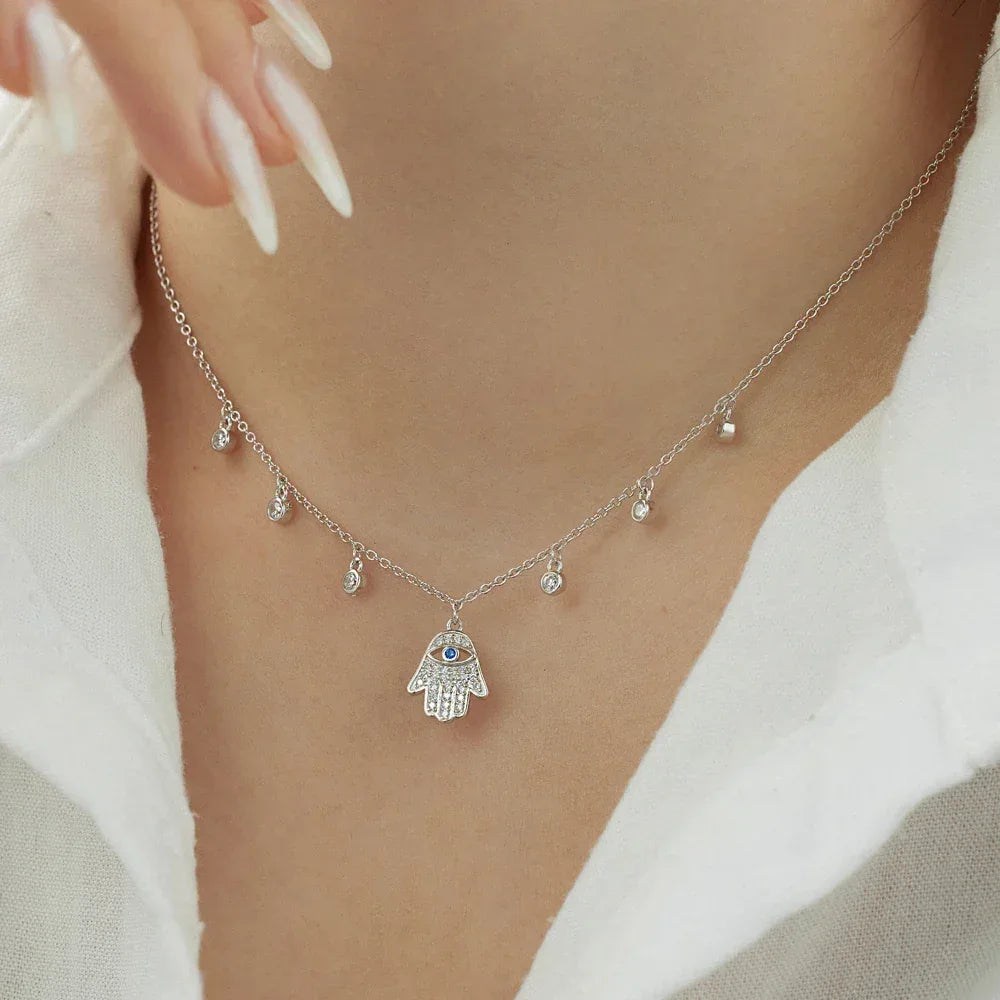 Silver link necklace with hamsa hand pendant, blue eye detail, and small crystal drops