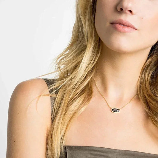 Gold-tone necklace with small oval pendant at the base of a woman’s throat.