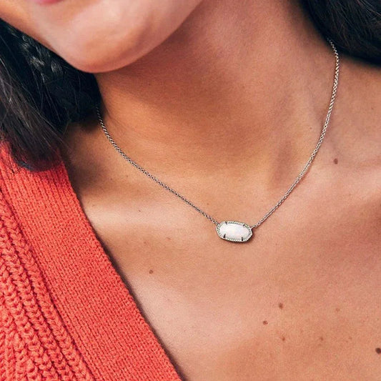 Silver-tone necklace with oval pendant on a woman’s neckline, paired with a red knit top.