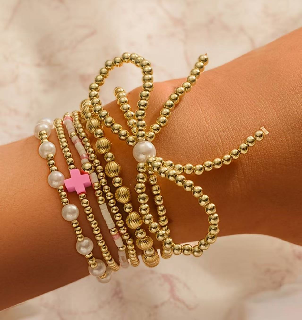 Gold-tone beaded bracelets with faux pearls and pink cross charm, stacked on wrist