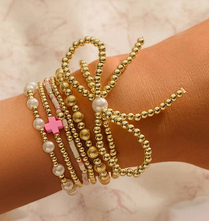Gold-tone beaded bracelets with faux pearls and pink cross charm, stacked on wrist