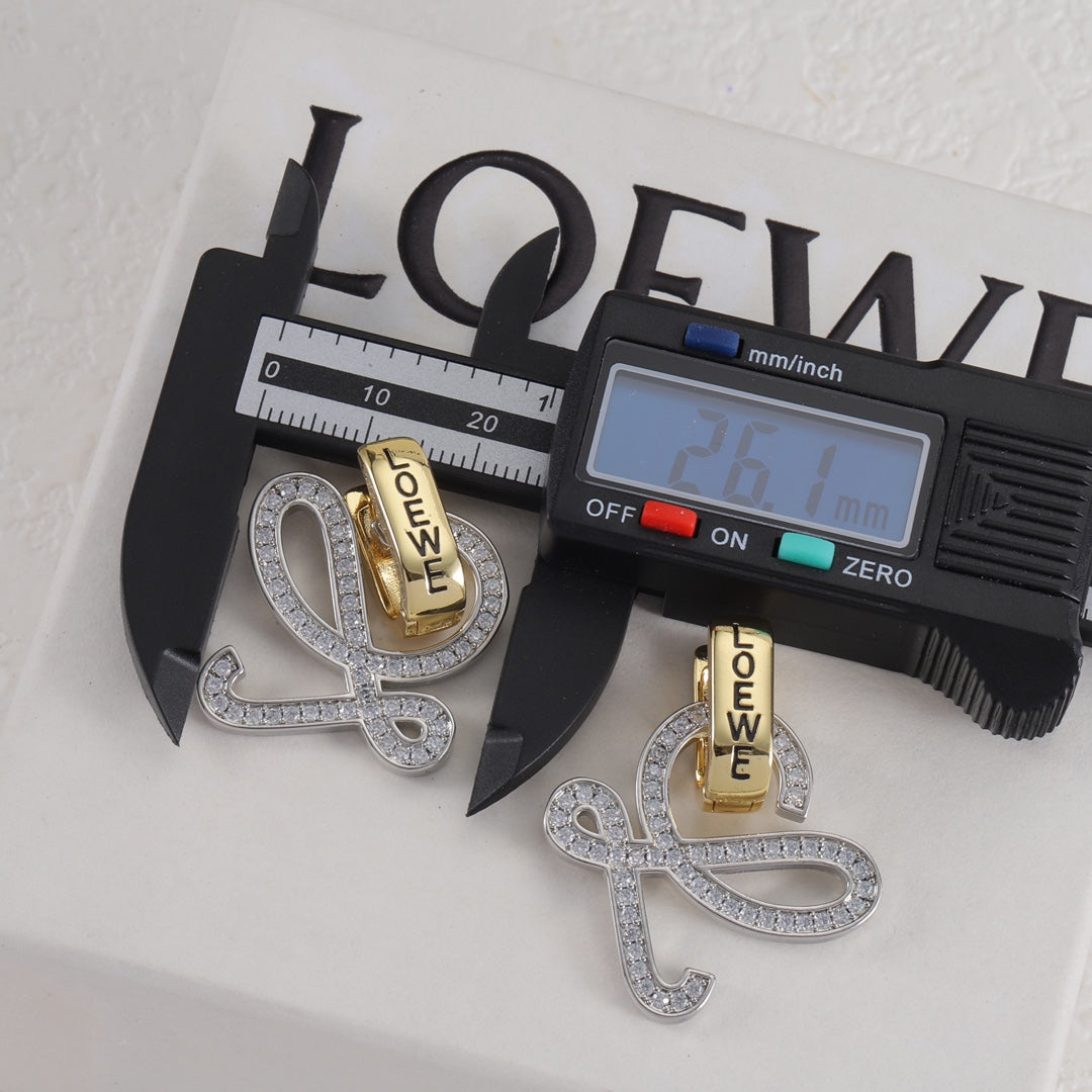 Gold and silver logo stud earrings with openwork outline and clear stones; caliper for scale