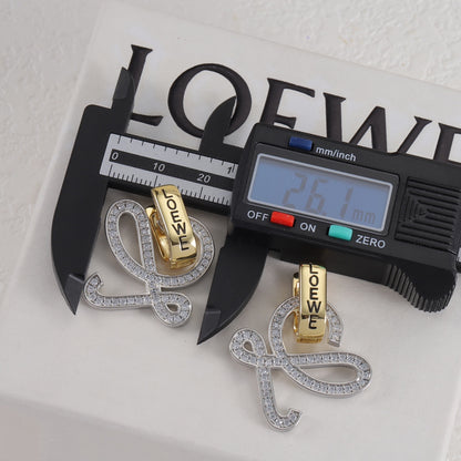 Gold and silver logo stud earrings with openwork outline and clear stones; caliper for scale
