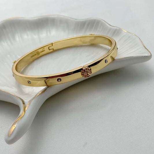 Gold hinged bangle with logo engraving, small crystal stones, and charm clasp