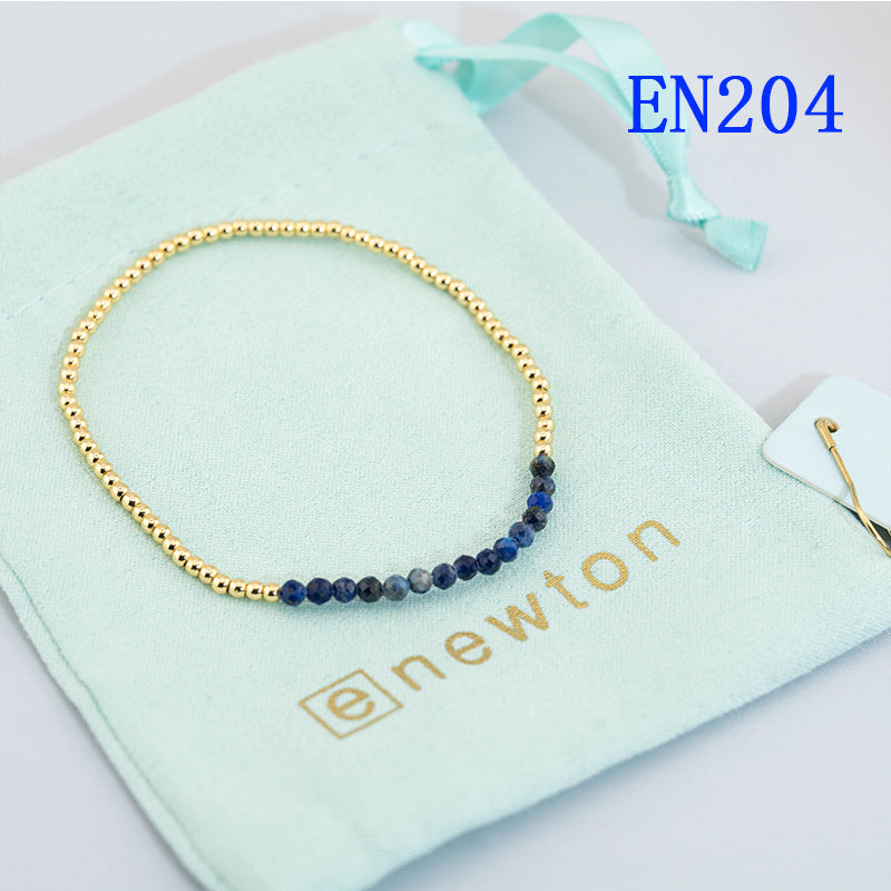 Elastic beaded bracelet with gold round beads and a deep blue bead accent row.
