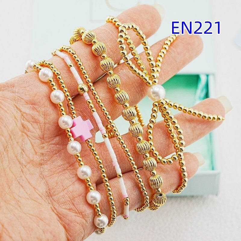 Gold-tone beaded bracelets with faux pearls and pink cross charms on open palm