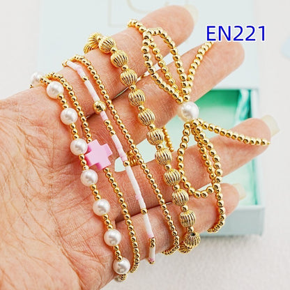 Gold-tone beaded bracelets with faux pearls and pink cross charms on open palm