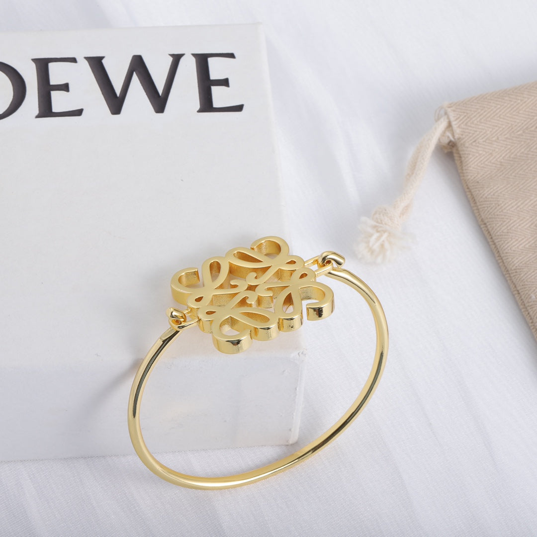 Gold open cuff bracelet with hinged cuff and cutout logo centerpiece detail