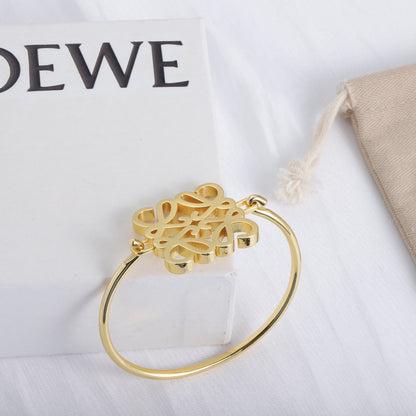 Gold open cuff bracelet with hinged cuff and cutout logo centerpiece detail