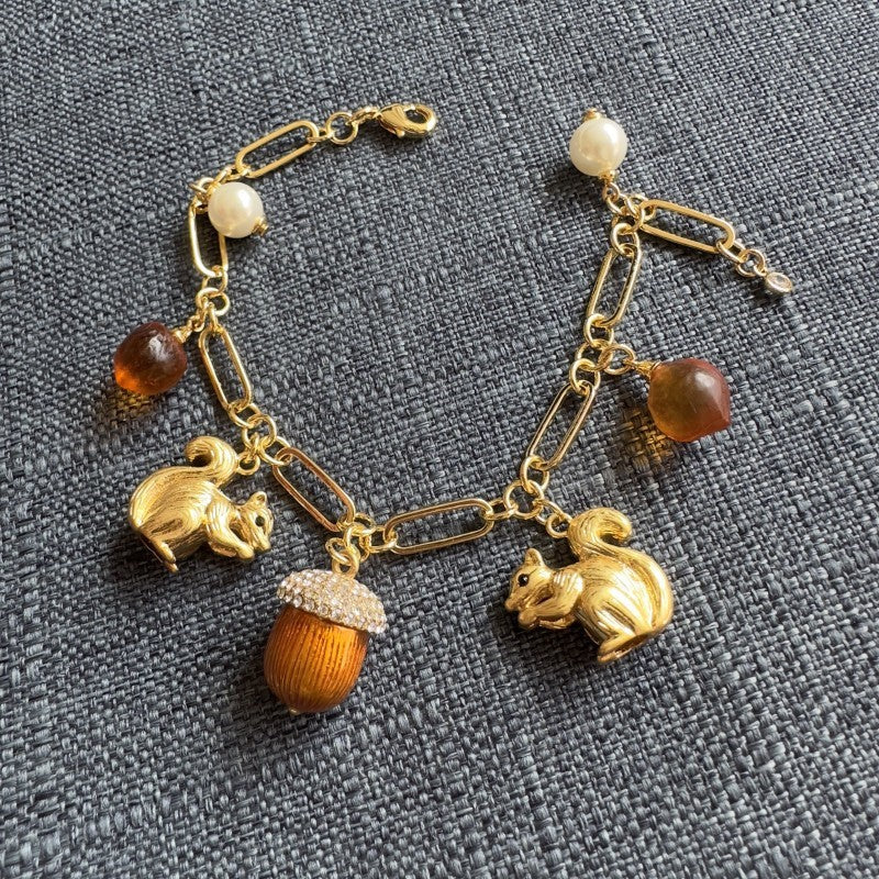 Gold-tone charm bracelet with squirrel, acorn, and pearl beads on link chain