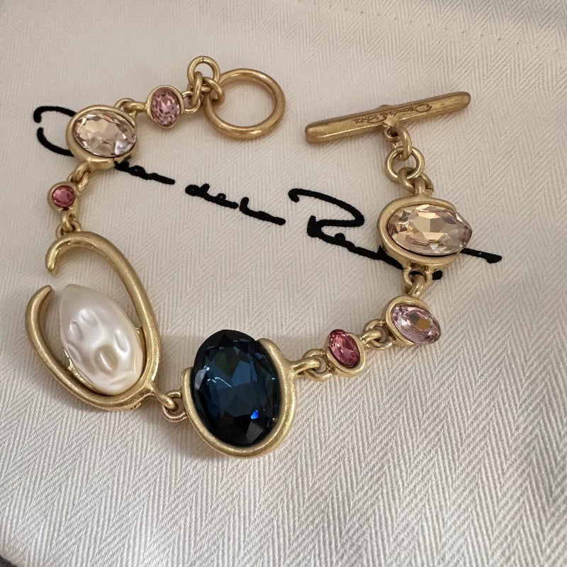 Gold-tone crystal and pearl O-ring bracelet with dark blue oval center and pink crystals