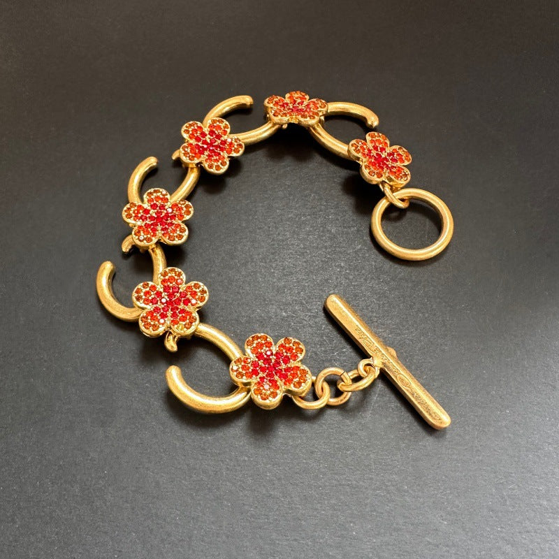 Gold-tone bracelet with red flower charms, pave stones, and bar toggle clasp