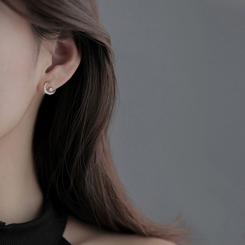 Moon and star diamond stud earrings in silver tone, worn on ear
