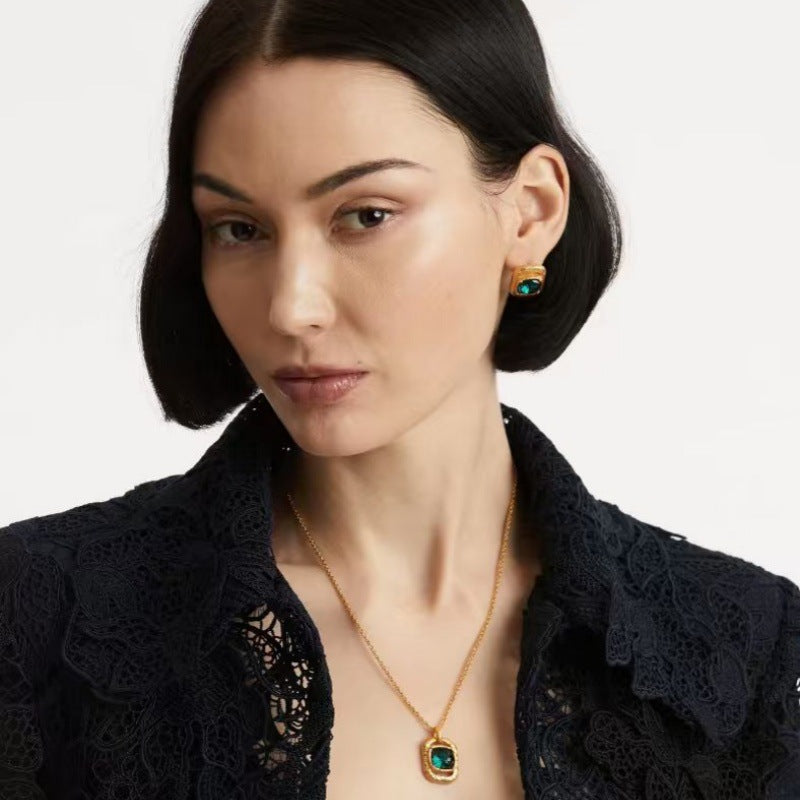 Hammered square pendant necklace with teal-blue faceted gemstone; gold chain worn