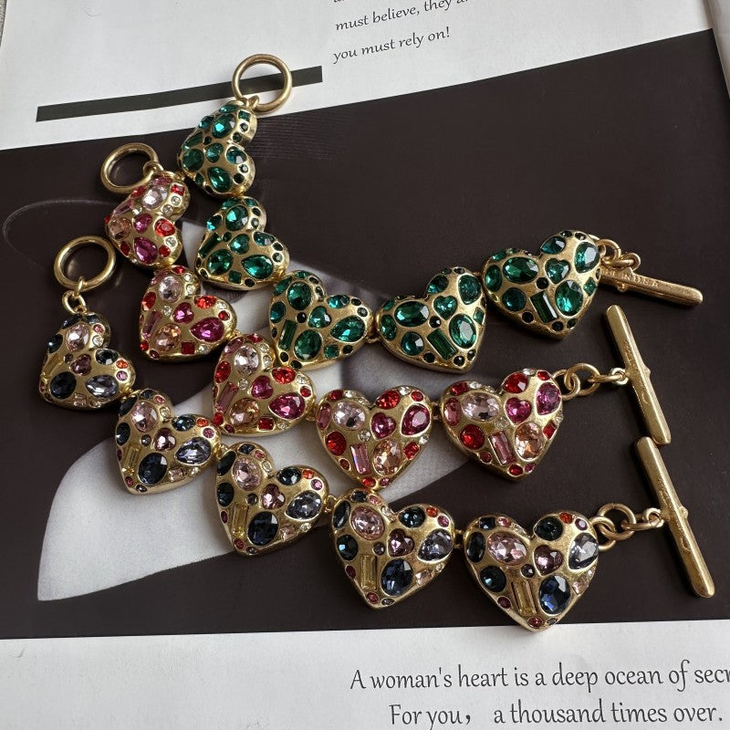 Gold-tone heart charm bracelet with pink and green gemstone accents and toggle bar