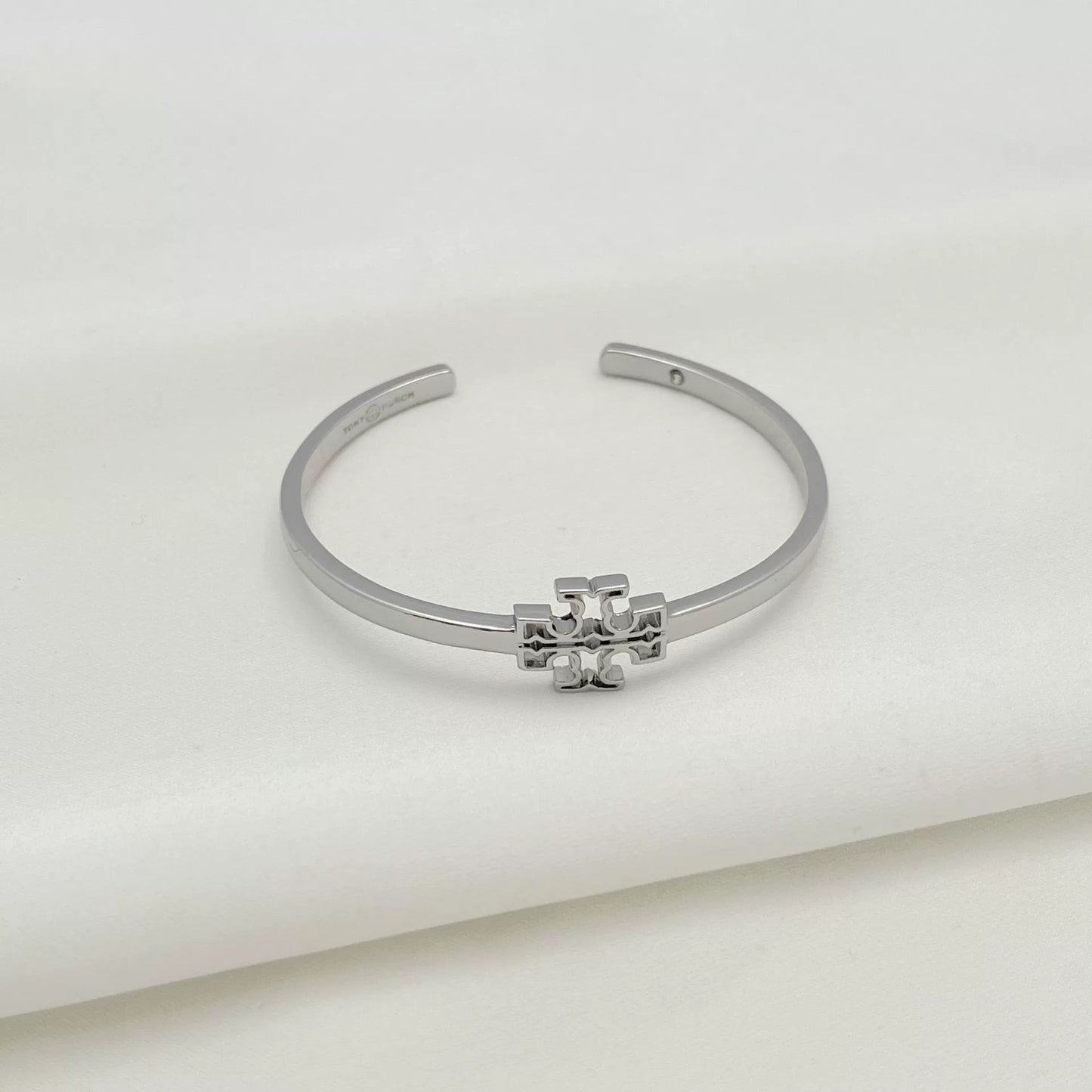 Openwork square logo smooth metal bangle, silver tone with central emblem detail