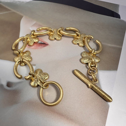 Gold-tone bracelet with floral charms, open-link chain, and long bar toggle clasp