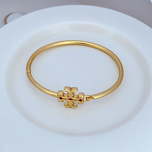 Gold open metal logo bangle with sculpted emblem centerpiece