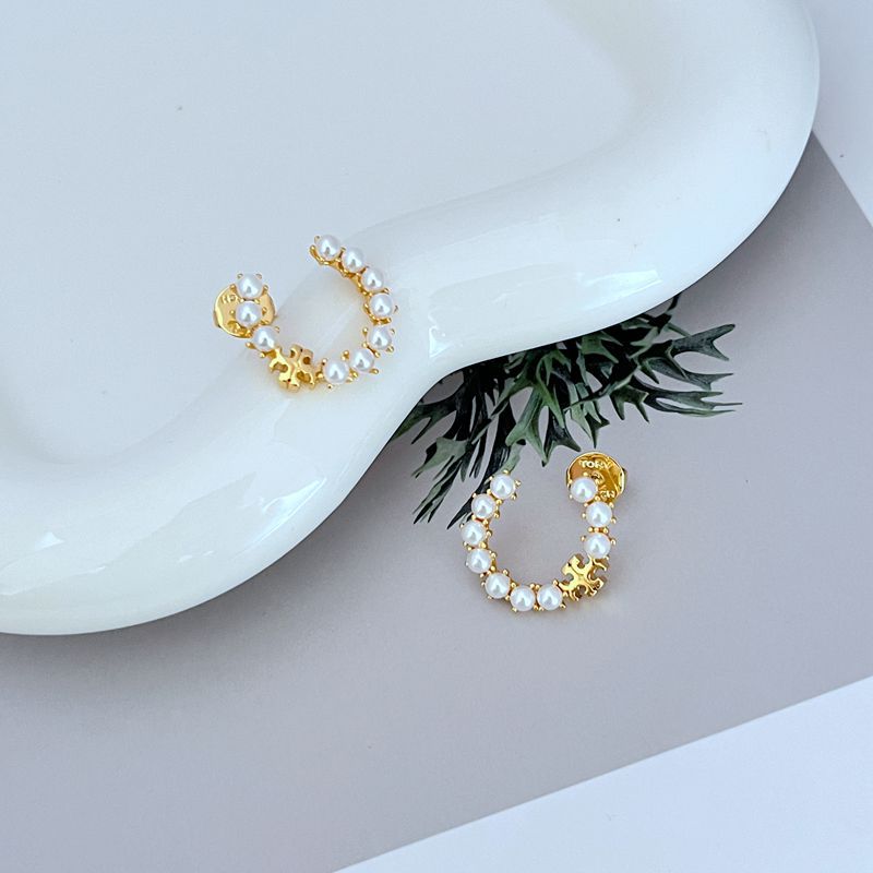 Gold C-hoop earrings with white pearl clusters and logo emblem; side view
