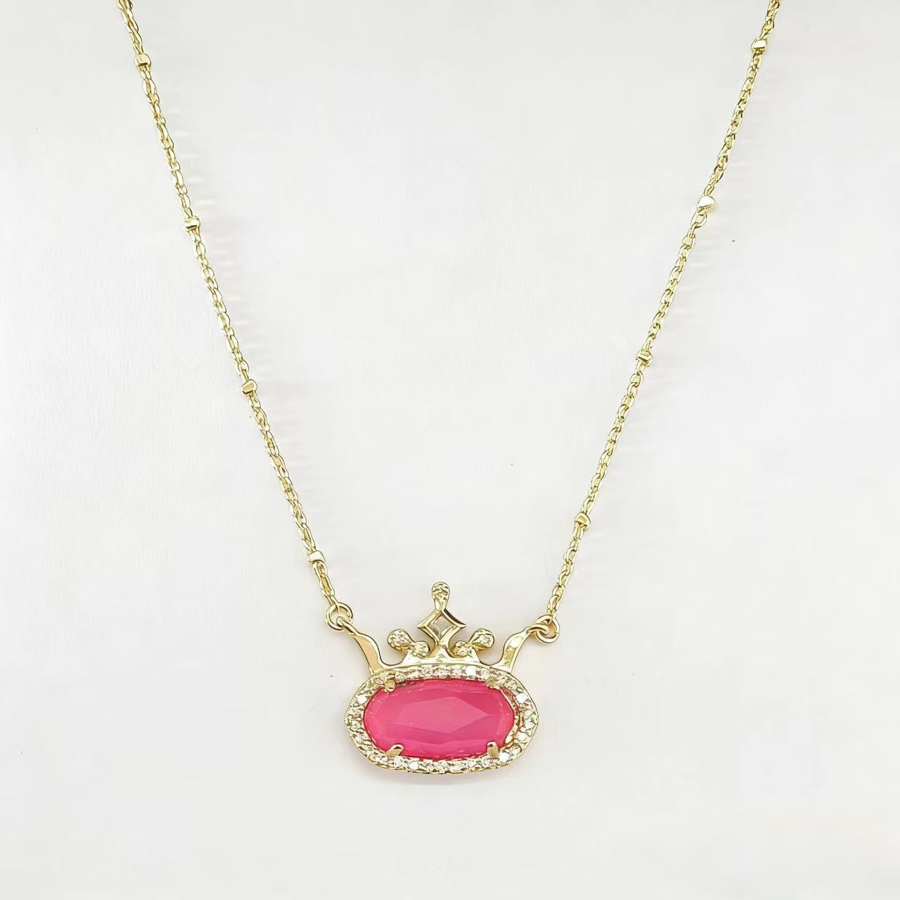 Gold-plated princess crown necklace with pink oval gemstone and diamond-style halo