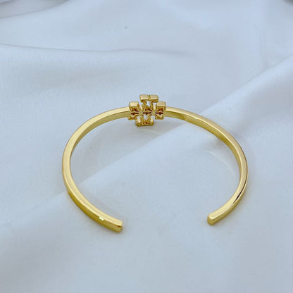 Gold tone open metal cuff bangle with square logo emblem at center