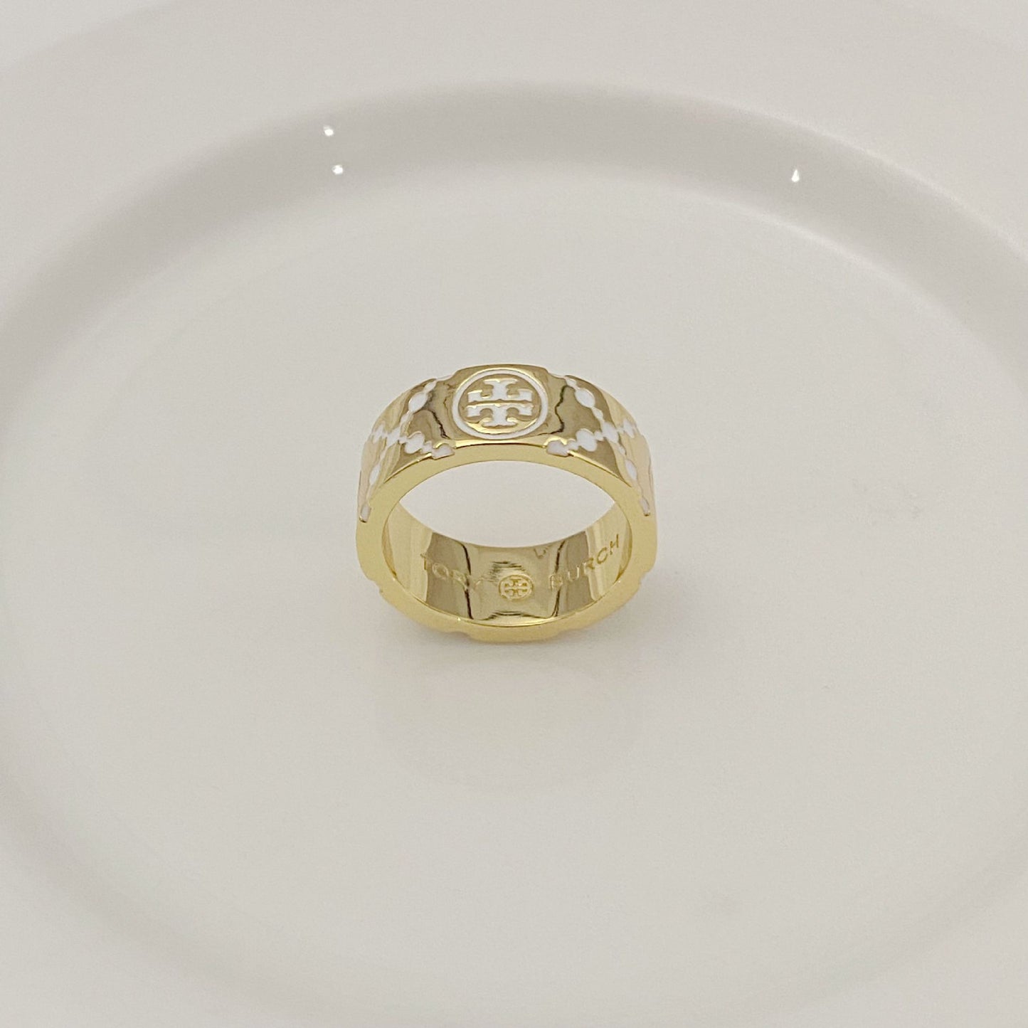 Gold-tone round metal ring with white enamel floral pattern and logo medallion