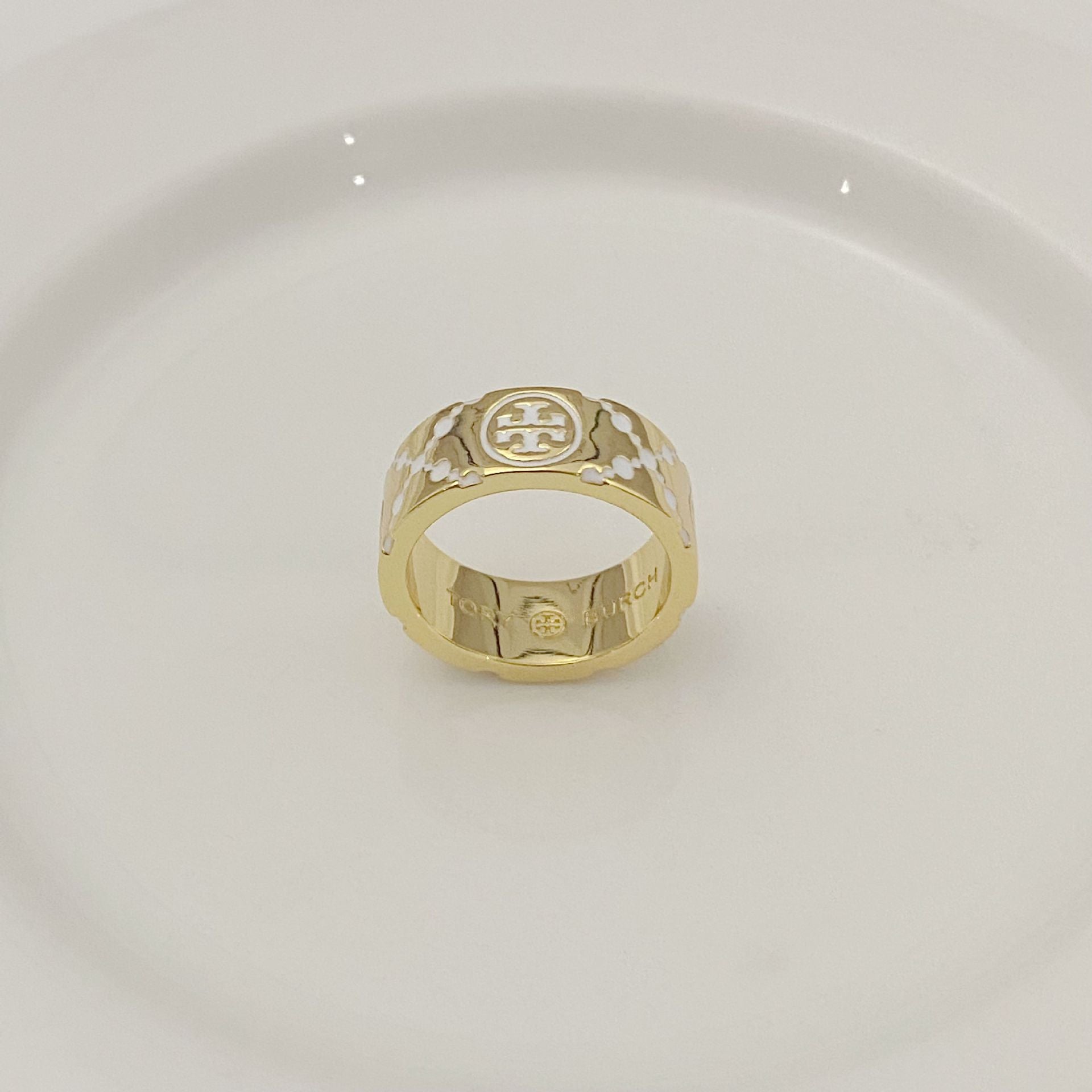 Gold-tone round metal ring with white enamel floral pattern and logo medallion