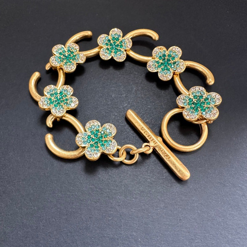 Gold-tone bracelet with green flower charms, pave stones, and bar toggle clasp