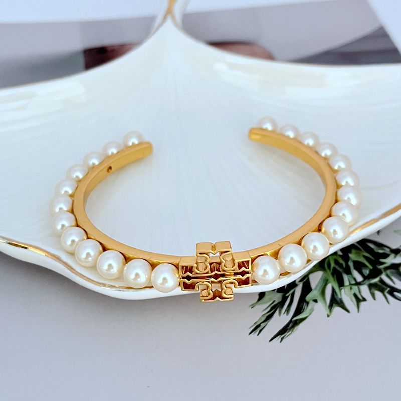 Gold open bangle with white pearls and square logo medallion in red enamel