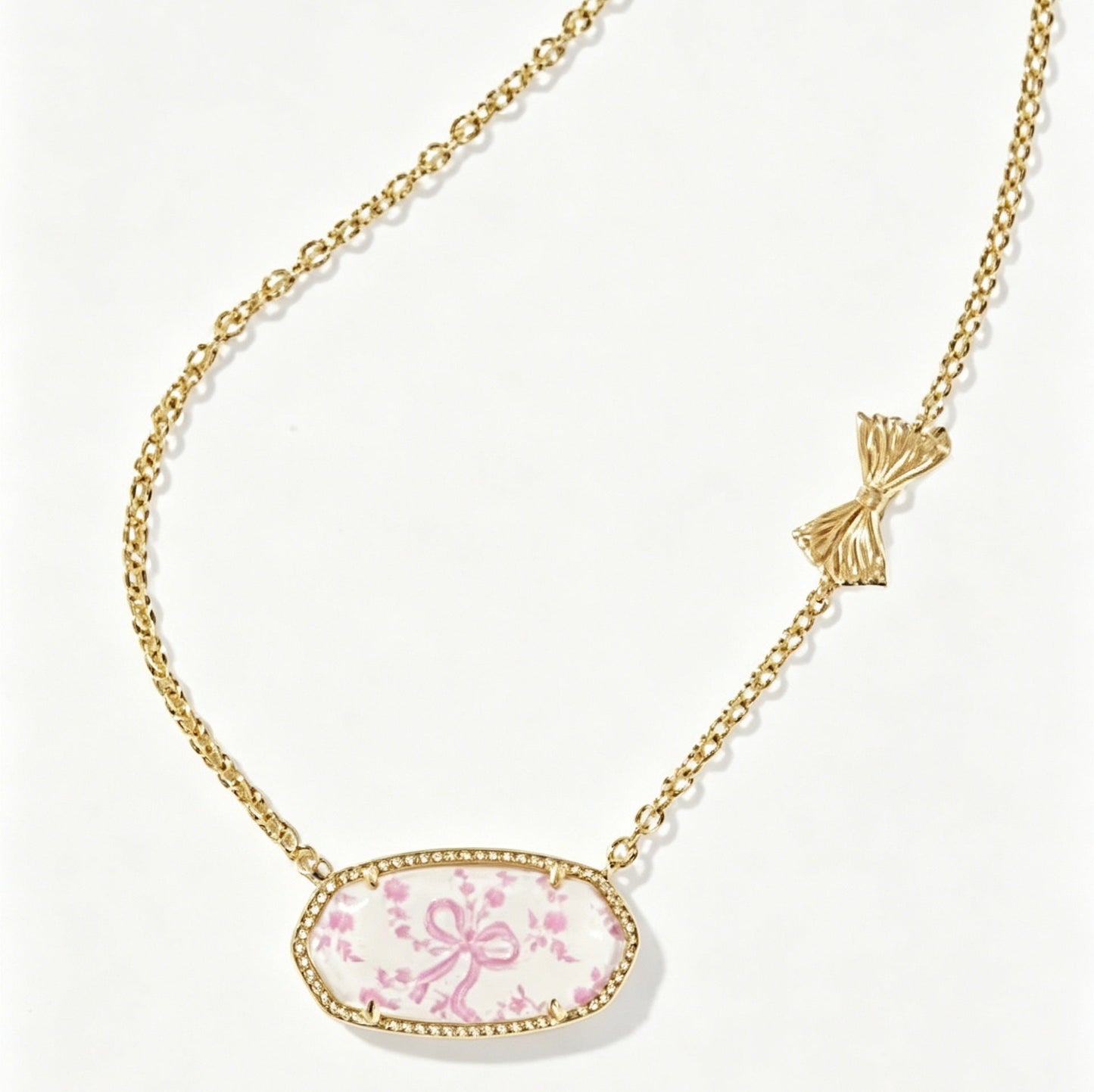 Gold-tone oval pendant necklace with pink floral cabochon and bow accent