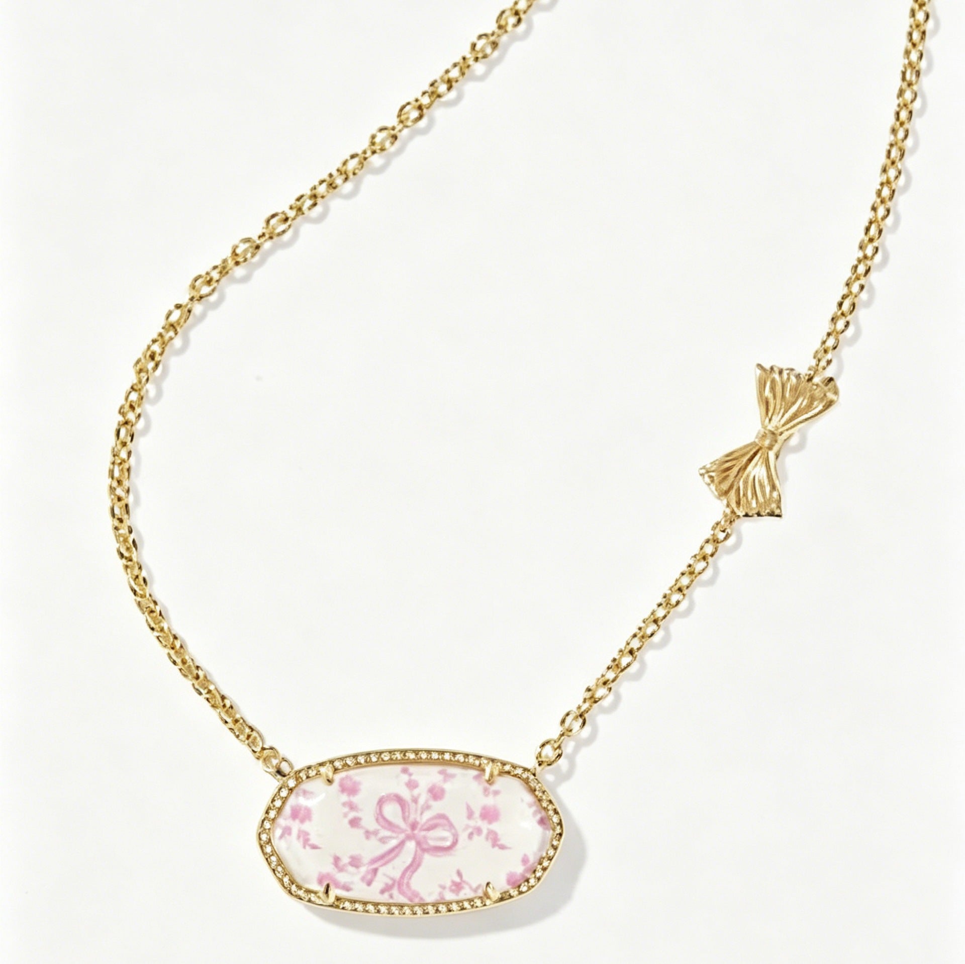 Gold-tone oval pendant necklace with pink floral cabochon and bow accent