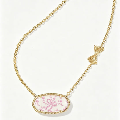 Gold-tone oval pendant necklace with pink floral cabochon and bow accent