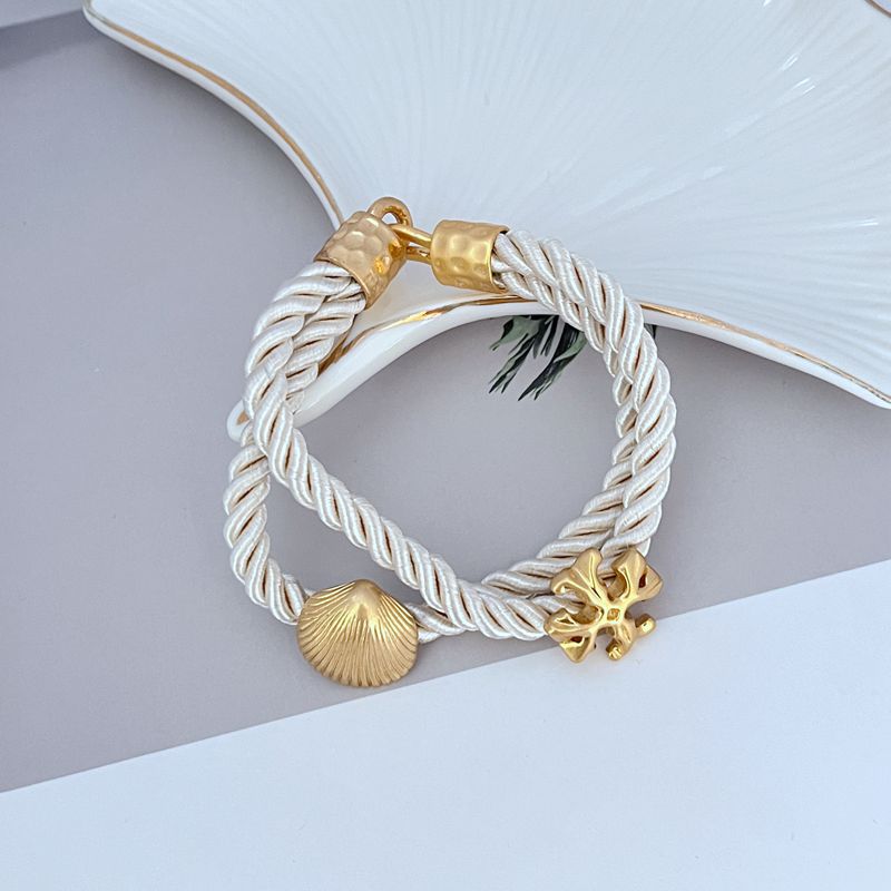 White braided cord bracelet with gold shell charm and logo toggle clasp
