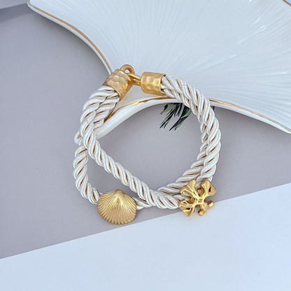 White braided cord bracelet with gold shell charm and logo toggle clasp